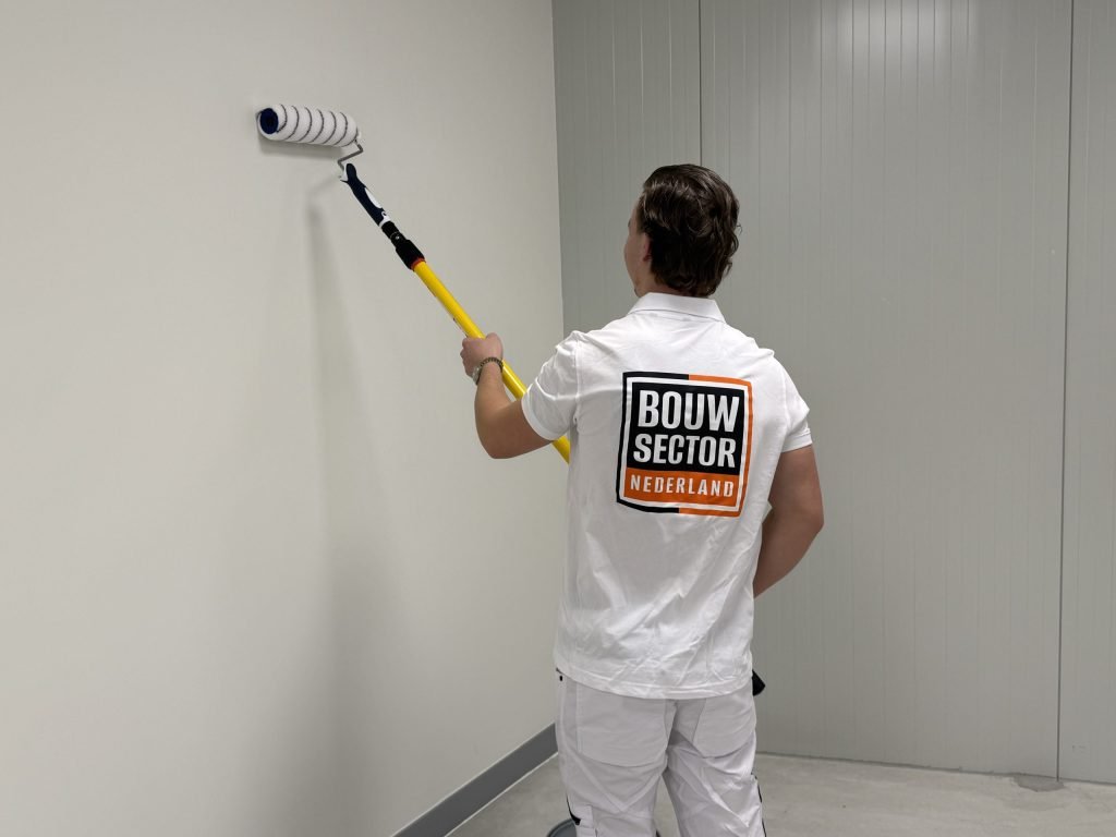 Schilder van Bouwsector Nederland rolt een lichte wand met een roller op een verlengsteel